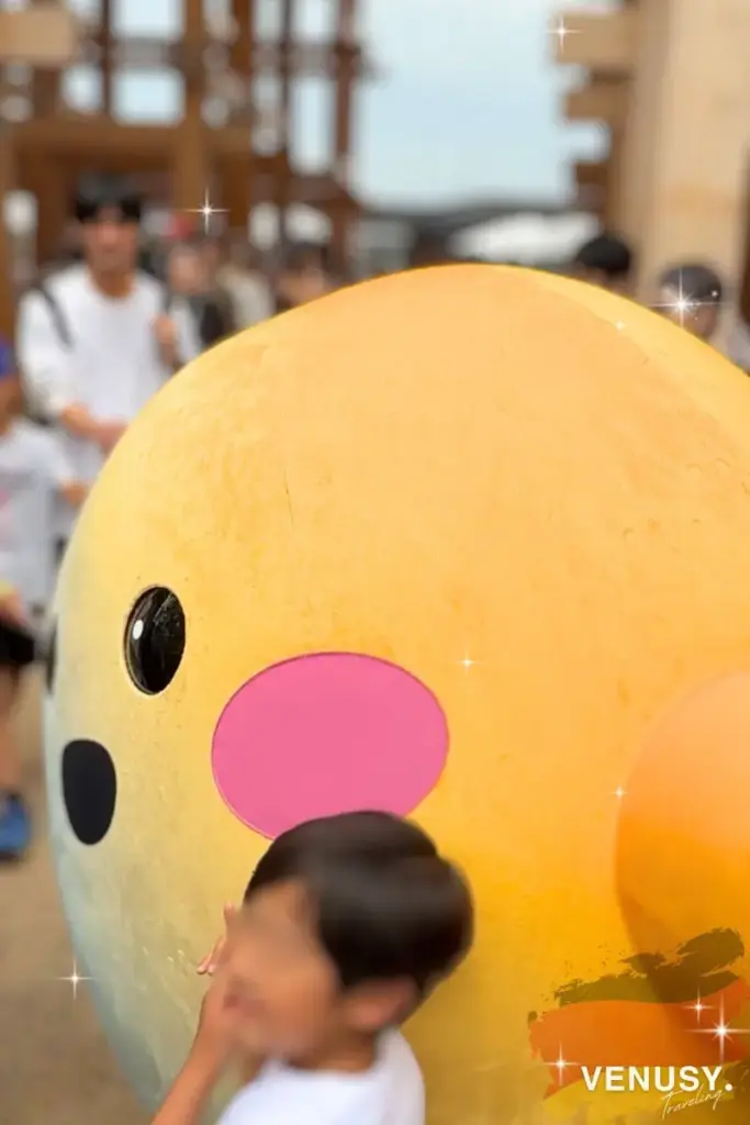 ドイツ館前で人に囲まれているサーキュラーちゃんと、ぎゅっとくっつく子どもの姿(大阪万博2025)