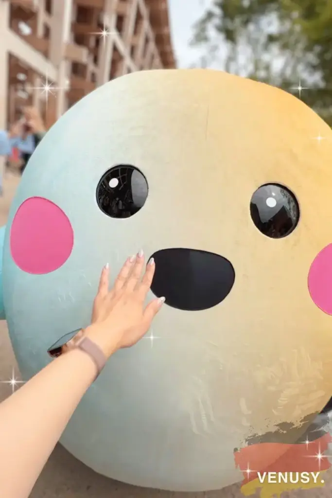 ヴィナぽ♡が大阪・関西万博ドイツ館の公式キャラクター「サーキュラーちゃん」にそっと手を伸ばして再会のタッチをしているシーン
