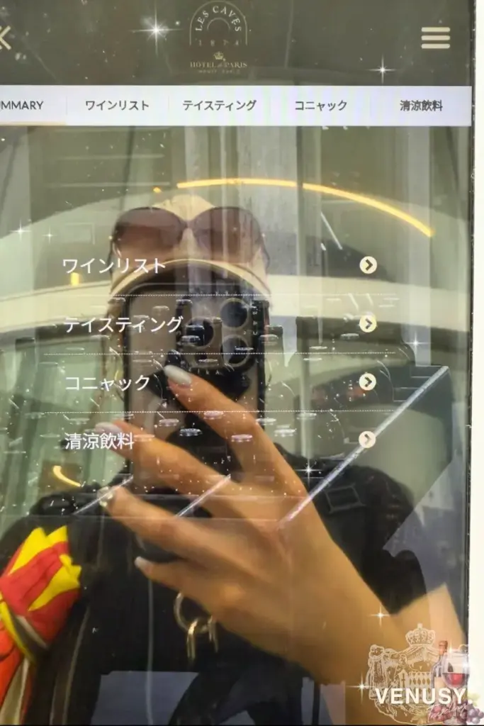 モナコ館ワインバーのワインリスト画面(タブレット端末)と反射に映る来場者の様子 | Wine menu screen at Monaco Pavilion wine bar with guest reflection – Expo 2025 Osaka
