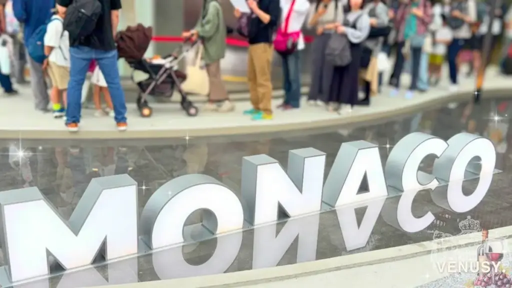 大阪・関西万博モナコ館のロゴサインと、行列に並ぶ来場者の様子 | Monaco Pavilion illuminated sign and visitors queuing at Expo 2025 Osaka