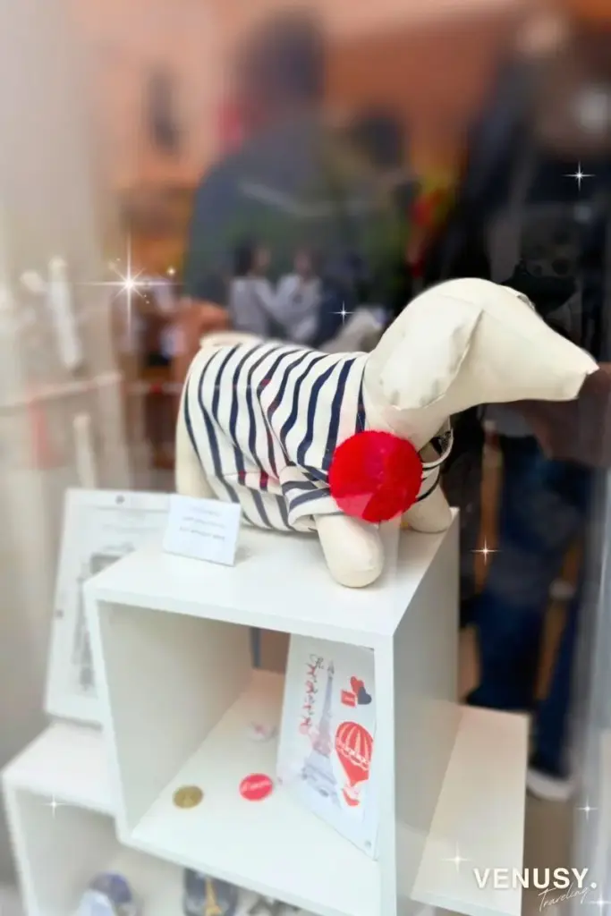 大阪万博フランス館のお土産ショップに並ぶ犬のぬいぐるみ。白地に青い服を着たデザイン。