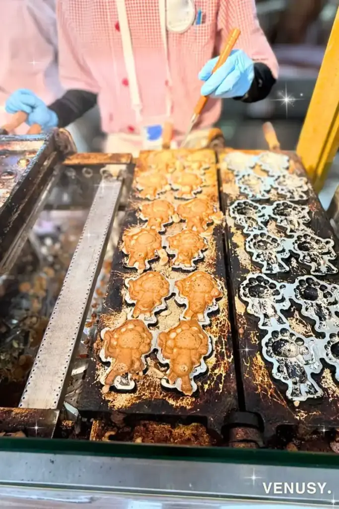 焼き立てミャクミャク焼き実演シーン：大阪・関西万博2025のJAPANマルシェで、型に流し込まれた生地が次々と焼き上がっていくミャクミャク焼きの実演シーン。香ばしい香りと熱気が漂う様子が伝わる写真。