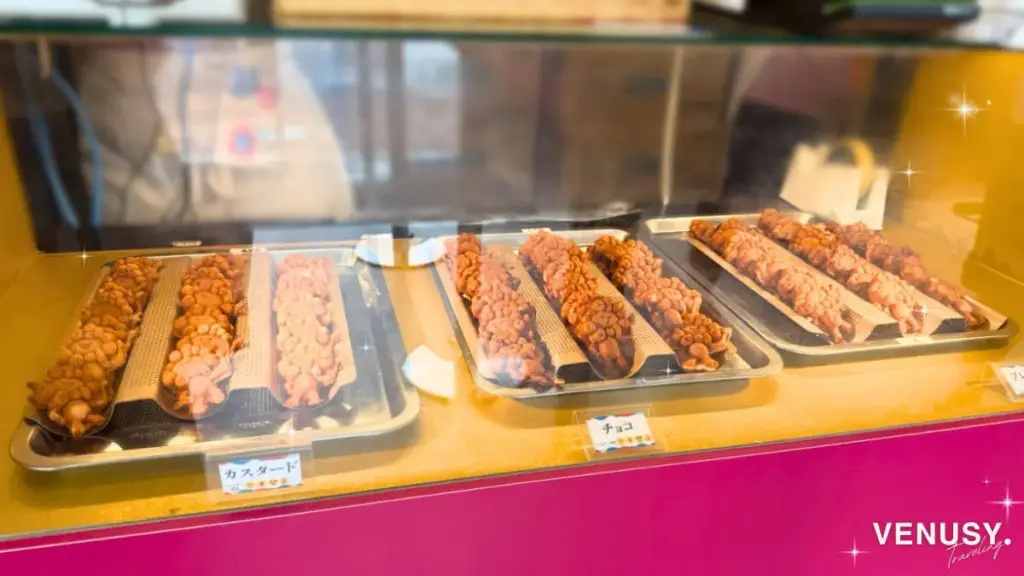 大阪・関西万博2025 東ゲート店舗で並ぶミャクミャク焼き全種類（プレーン・カスタード・チョコ）がずらりとトレーに並ぶ様子