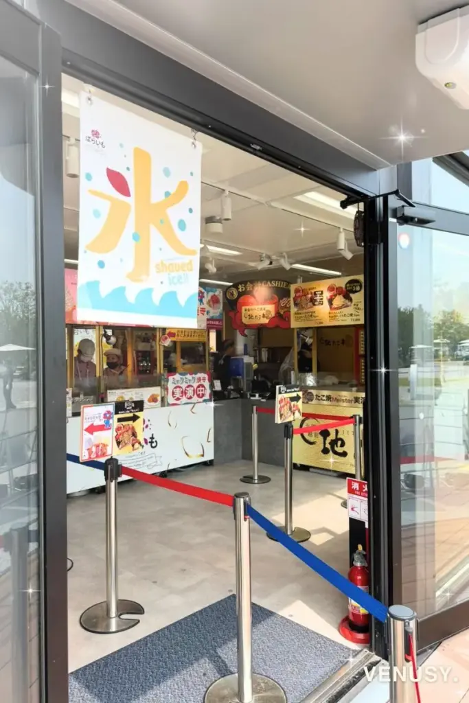 大阪・関西万博2025 東ゲートのJAPANマルシェ内ばらいも店舗に掲げられた「氷 shaved ice!!」ののぼり旗。夏場は万博ミャクミャク焼きソフトクリームと並んでかき氷も人気。