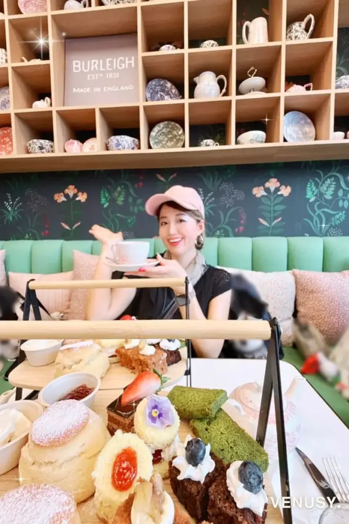 大阪万博イギリス館アフタヌーンティーを楽しむヴィナぽ♡｜紅茶を手に店内の可愛い壁前で微笑む様子