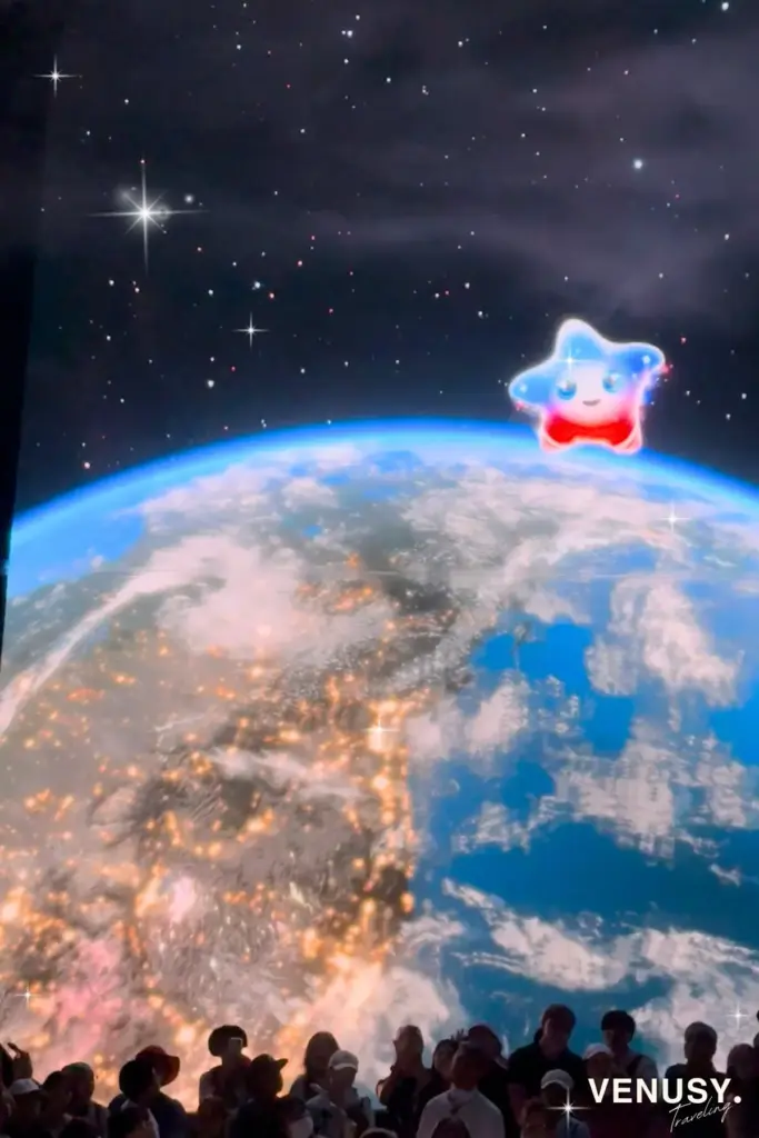 大阪万博アメリカ館で地球の上を飛び回る公式キャラクターSparkちゃんと、それを見上げる来場者たち