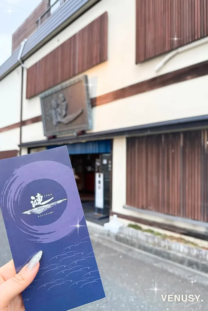 鳥羽の人気店『漣（さざなみ）』のパンフレットを手に撮影した写真。背景には店舗外観がやさしくぼけて映っている。
Pamphlet of Sazanami in Toba with the restaurant exterior softly blurred in the background